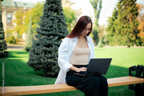 Woman works on laptop while sitting on bench in green park on sunny day