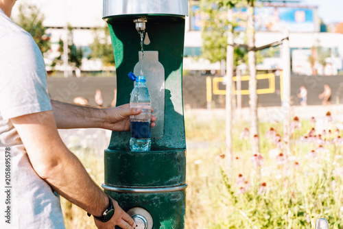 Fotografía Eco-minded man refilling reusable plastic bottle at outdoor water fountain