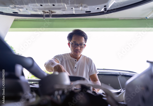 View through channel and shade. A man wearing glasses is open car hood to check its readiness and to make sure there are no abnormalities in engine before driving.