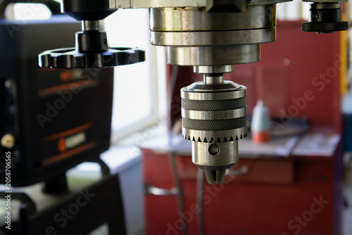 Close-up of a metal drill chuck on an industrial vertical drilling machine