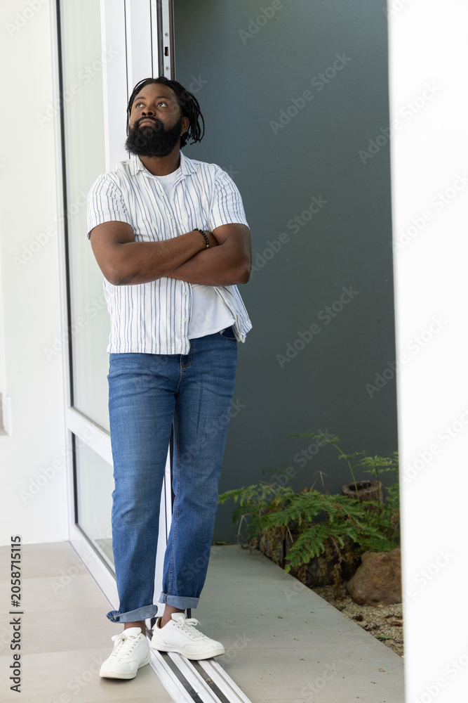 Obraz premium African American man leaning in doorway by sliding door wearing striped shirt jeans sneakers