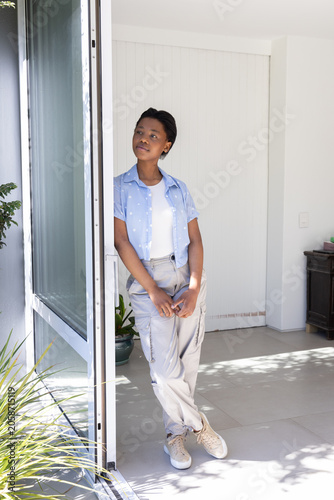 Картината върху платно African youth female standing and leaning in home entryway by sliding door weari
