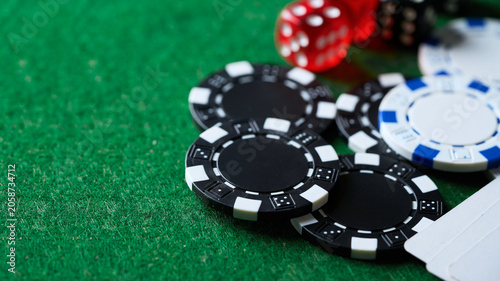 Close-up of black and blue poker chips with red dice on green felt casino table background. Selective focus on gambling tokens for betting games with copy space.