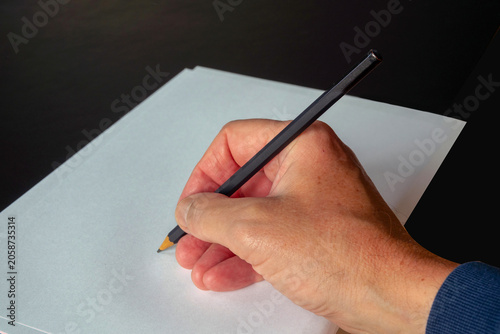 A hand with a pencil on a piece of white blank paper. Image with copy space.