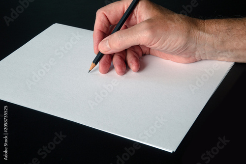 A hand with a pencil on a piece of white blank paper. Image with copy space.