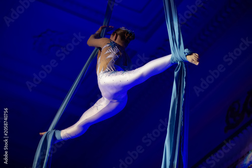 Dancer performs aerial silk act in a theater with blue lighting during an evening show