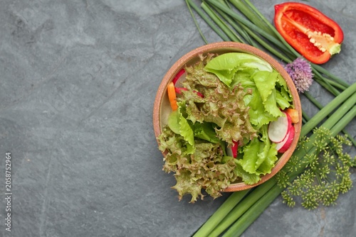 Fresh lettuce of different kinds served in the bowl on stone table, top view. Healthy lettuce salad, radish and carrot.