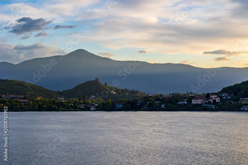 Village of Avigliana dominated by the ruins of its medieval castle at sunrise, seen from the opposite bank of the Lago Grande di Avigliana