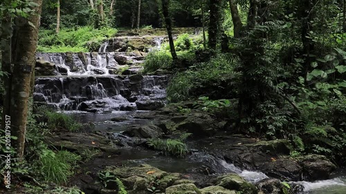 The video background features a natural landscape of a waterfall in a lush forest. Sam Lan Waterfall in Saraburi National Park boasts beautiful flowing water surrounded by diverse flora.