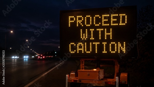 A mobile highway sign at night warning motorists to proceed with caution