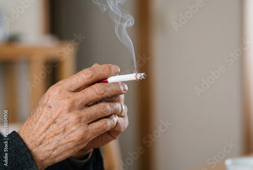 Wrinkled hand of an elderly man holding a lit cigarette with smoke