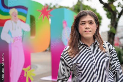 Thai transgender woman standing in front of a colorful Pride sign outdoors