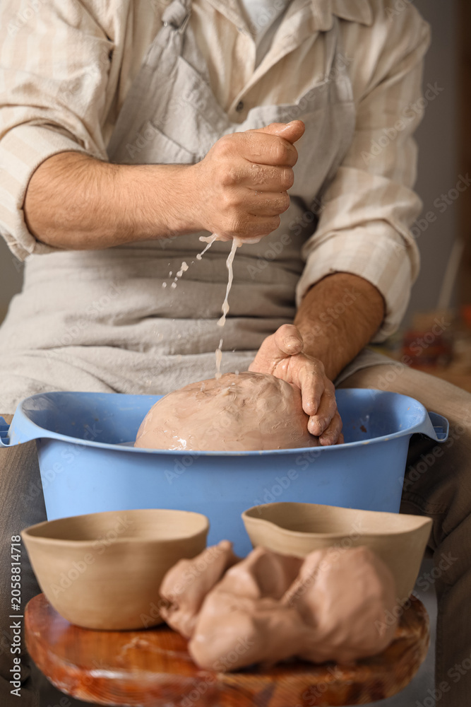 Fototapeta premium Potters hands squeezing water from clay in blue basin, pottery crafting process, ceramic art workshop
