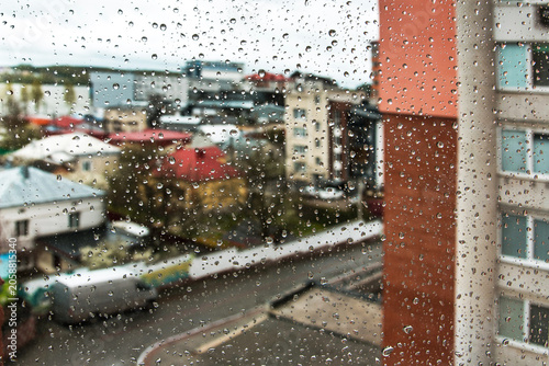Rain drops on window glass with blurred city background and copy space