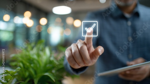 Businessman interacts with digital checkmark icon on touchscreen device while working in modern office environment with plants and blurred background