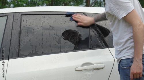 A man washes the car windows with a cloth before applying an anti-rain coating.