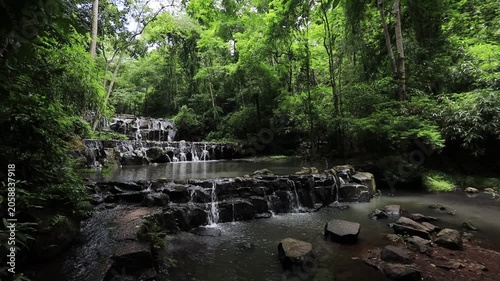 The video background features a natural landscape of a waterfall in a lush forest. Sam Lan Waterfall in Saraburi National Park boasts beautiful flowing water surrounded by diverse flora.