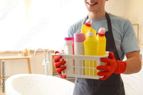 Young man with basket of cleaning supplies in bathroom, closeup