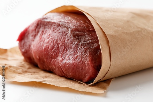 A raw, unprocessed cut of beef wrapped in brown butcher paper, presented on a white background.