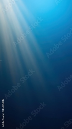 Sun rays shining through deep blue ocean water. Underwater view with light beams penetrating dark sea surface. Abstract background for World Oceans Day and marine conservation concept.