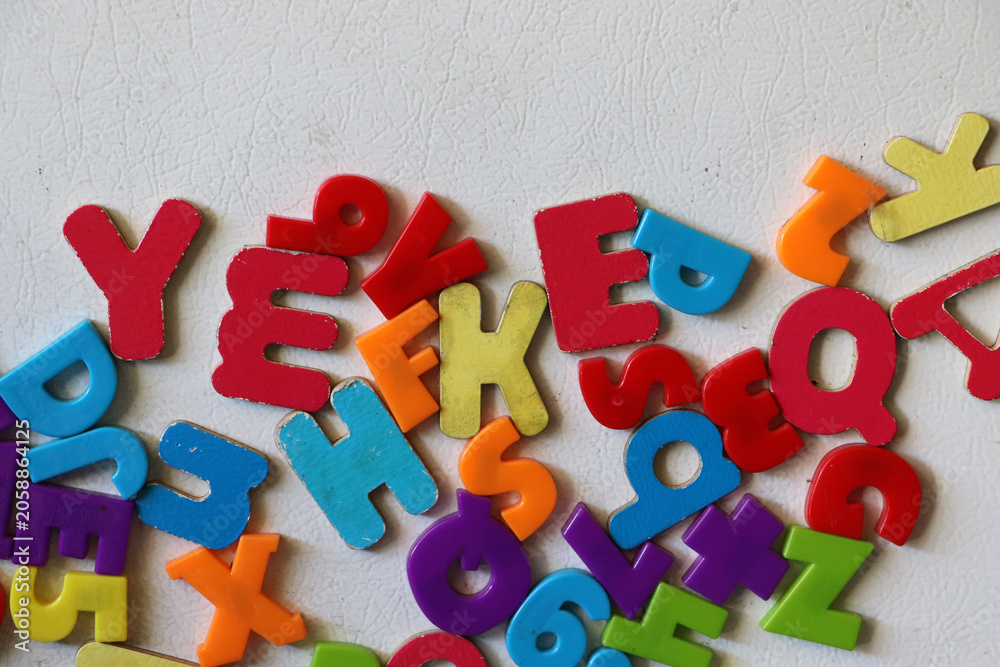 Fototapeta premium Vibrant and colorful plastic magnetic alphabet letters piled together in a chaotic design layout on a solid white tabletop background