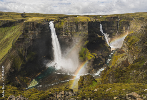 Εκτύπωση καμβά Spectacular double waterfall dropping into a steep green canyon with vivid rainbows forming in the mist