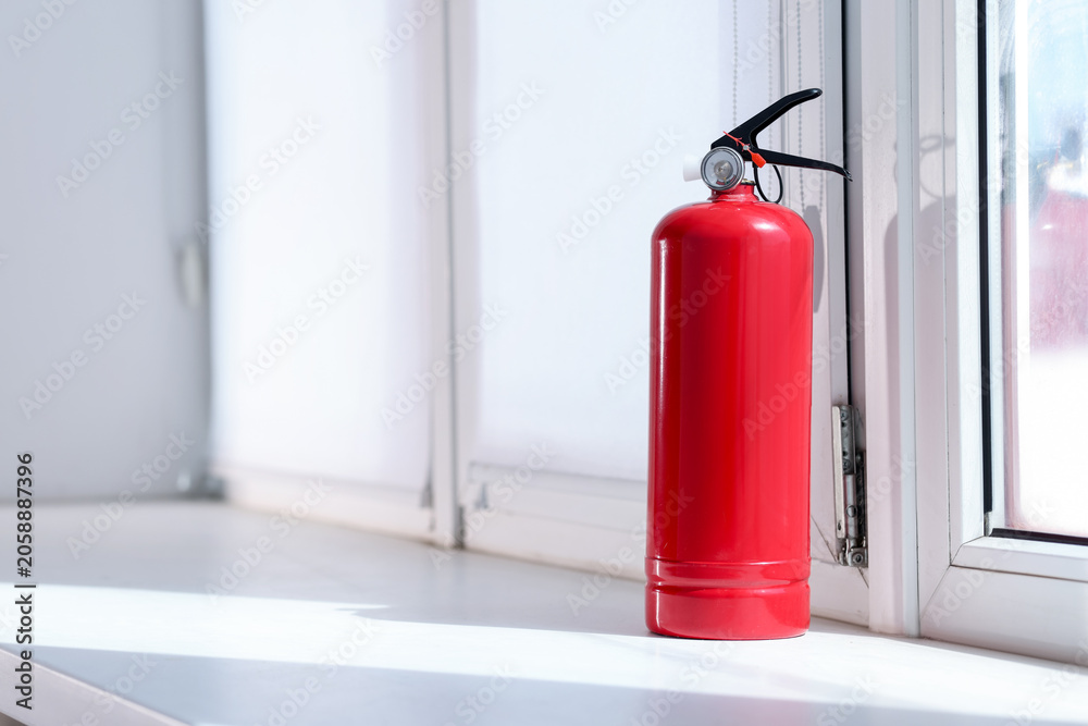 Fototapeta premium One red fire extinguisher near window indoors, space for text