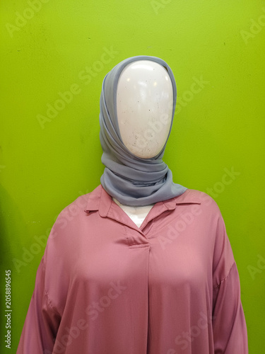 Female mannequin wearing grey hijab and dusty pink shirt blouse against plain bright green wall background. Front view close up of fashion retail display.