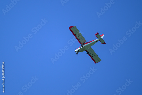 Petit avion de tourisme rouge et blanc à hélices  vu de dessous volant sur un ciel bleu