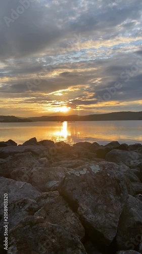 Rocky lakeshore at sunset with golden reflections on calm water under dramatic evening clouds in Finland