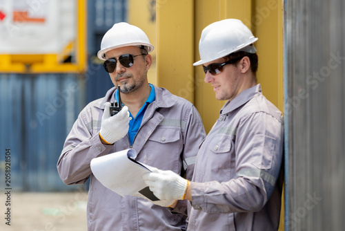 Bild auf Leinwand Two construction workers in safety helmets and uniforms review blueprints and communicate on-site outdoors