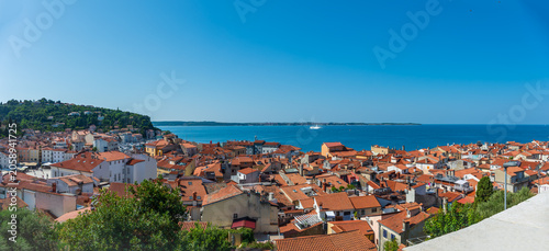Canvastavla Malerische Küstenstadt Piran mit roten Hausdächern und blauem Meer unter klarem Himmel