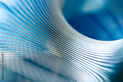 Close-up of shiny metal coils creating a dynamic wave pattern against a bright blue backdrop. Perfect abstract texture for industrial and corporate concepts. Photo