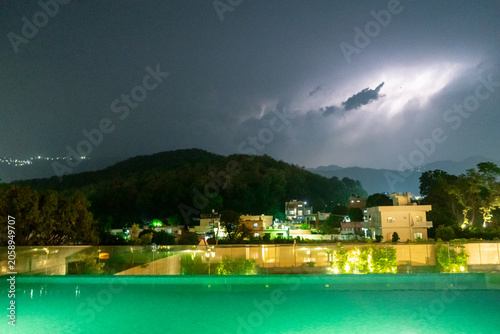Dehradun town with himalaya mountains in the distance with lightning strikes and cloudy monsoon weather with the hill station town of Mussoorie in the distance