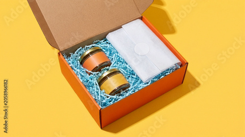Top view of an open corrugated cardboard gift box filled with artisanal fruit jam jars and blue shredded packing paper. Perfect for unboxing concepts, e-commerce delivery, packaging mockups.