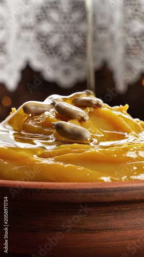 Vertical video: Sunflower oil pouring onto yellow pea puree porridge topped with sunflower seeds in a clay bowl. Healthy traditional rustic dish closeup footage for vegetarian cooking and organic food