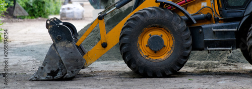 Photography Yellow backhoe loader parked on a dirt path with construction materials nearby
