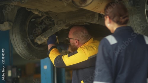 Caucasian male mechanic with glasses and a beard works alongside a female technician, reviewing a digital tablet and giving a thumbs-up. This high-energy commercial imagery represents gender diversity