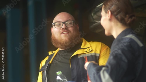 Caucasian male mechanic with glasses and a beard works alongside a female technician, reviewing a digital tablet and giving a thumbs-up. This high-energy commercial imagery represents gender diversity