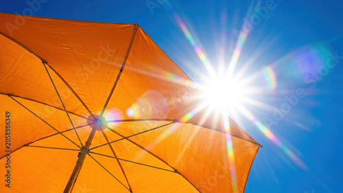 Bright sun flare over orange beach umbrella in clear blue sky, excessive heat, heatwave global warming