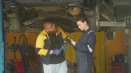 Caucasian male mechanic with glasses and a beard works alongside a female technician, reviewing a digital tablet and giving a thumbs-up. This high-energy commercial imagery represents gender diversity