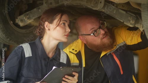 Caucasian male mechanic with glasses and a beard works alongside a female technician, reviewing a digital tablet and giving a thumbs-up. This high-energy commercial imagery represents gender diversity