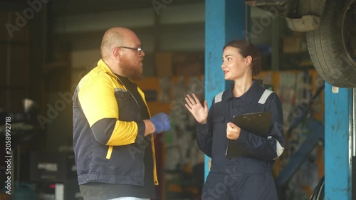 Caucasian male mechanic with glasses and a beard works alongside a female technician, reviewing a digital tablet and giving a thumbs-up. This high-energy commercial imagery represents gender diversity