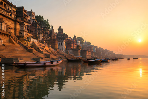Varanasi riverfront ghats at sunrise, boats on calm Ganges river, spiritual atmosphere