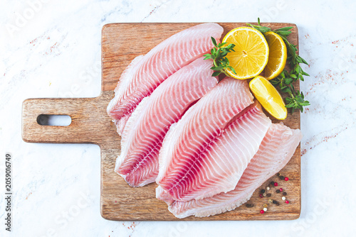 Fresh Tilapia fillet, on a wooden chopping board, with lemon and herbs, ready to cook in the kitchen, no people