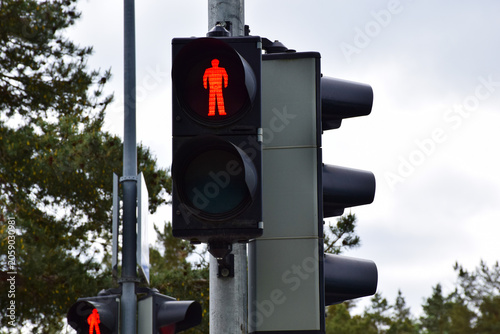 Fotografie Red pedestrian traffic light showing stop signal on a metal pole against a cloud