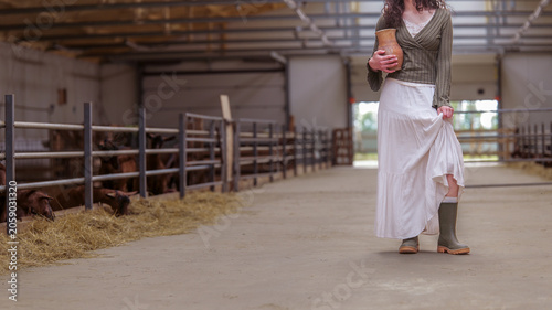 Photography Woman in long skirt and boots holding jug in barn with goats