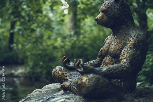 Bronze bear statue meditating on a rock in a lush green forest.