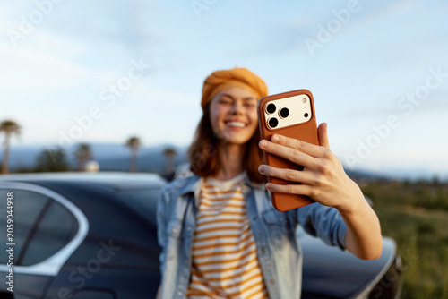 Foto Young woman on a casual road trip takes a selfie with a smartphone, smiling besi