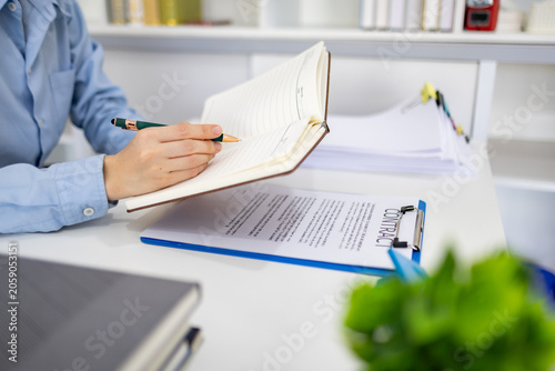 Hand writes checklist with focused calmness. Desk holds notebooks and clipboard. Person works quietly, task-oriented. Ideal for business, education, or planning visuals
